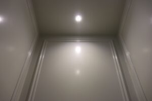 Upward view into a luxury residential elevator cab with rich wood grain paneling and multiple recessed ceiling lights
